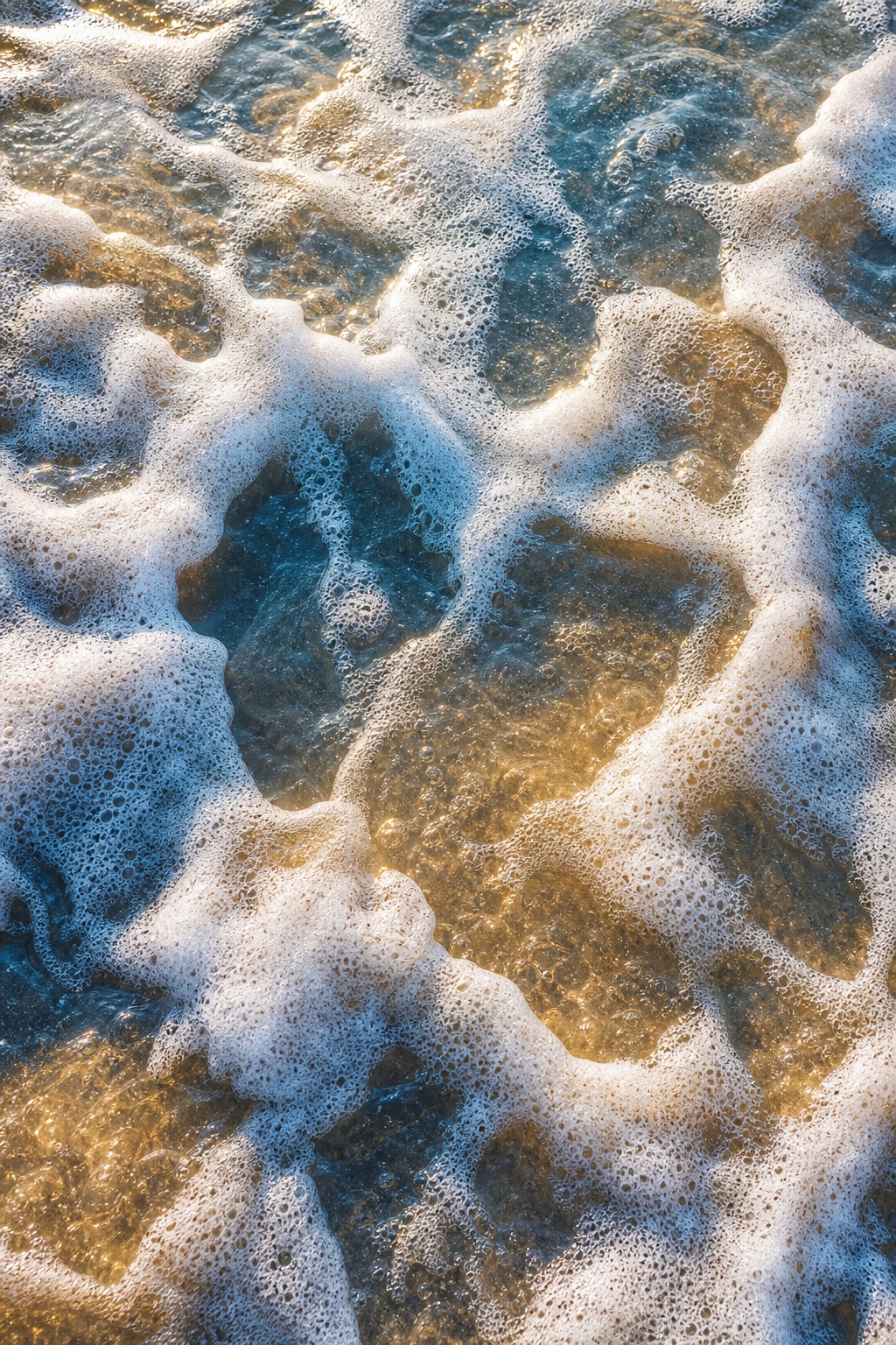 White sea foam breaking over golden coastal water in an abstract pattern