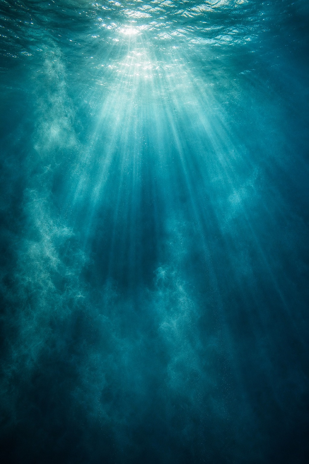 Teal underwater scene with bright light rays and drifting haze