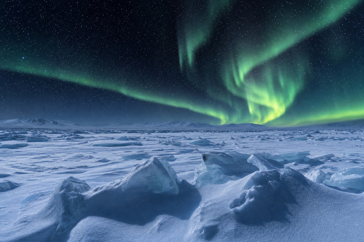 Green aurora lights over a frozen ice field with snow-covered ridges