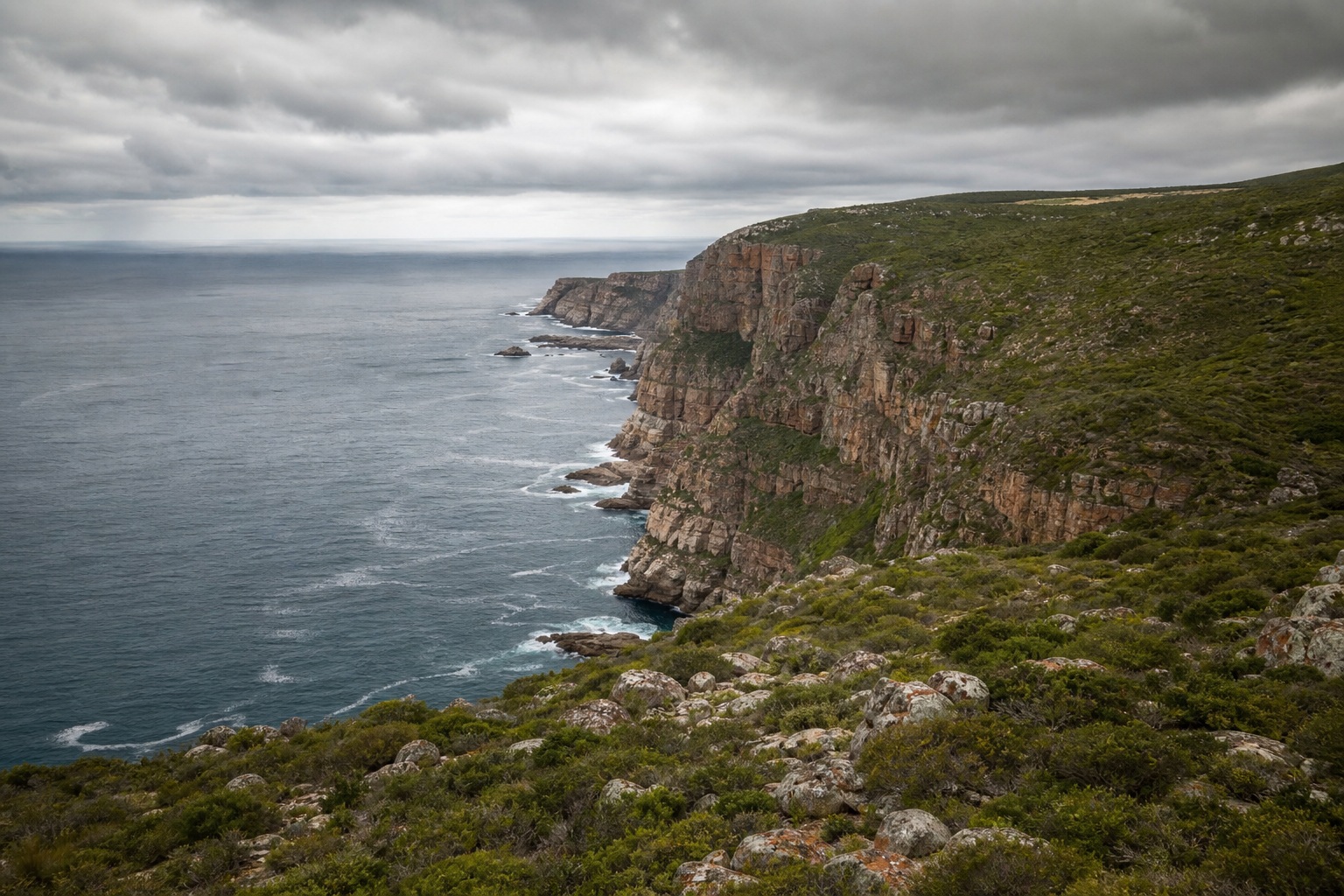 Rocky coastal cliffs overlooking a gray ocean under soft overcast skies.