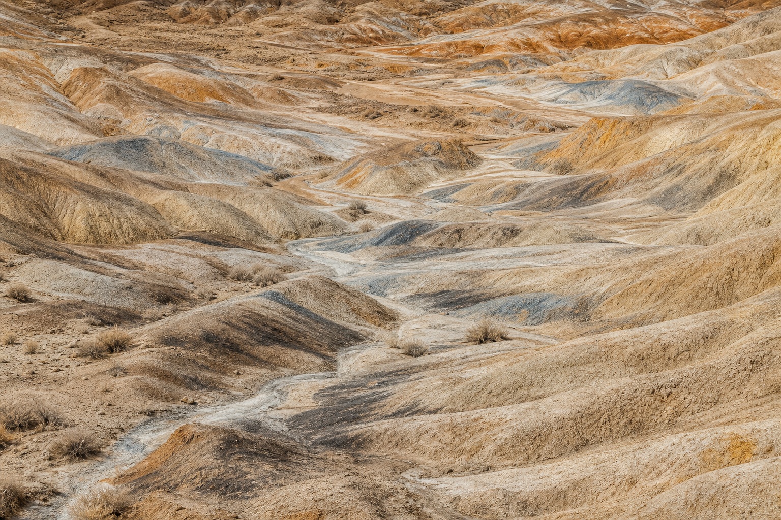 Eroded desert badlands with layered mineral gullies under clear noon light