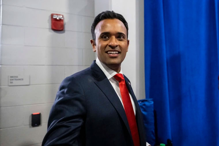 Business professional in a suit standing indoors beside a blue curtain