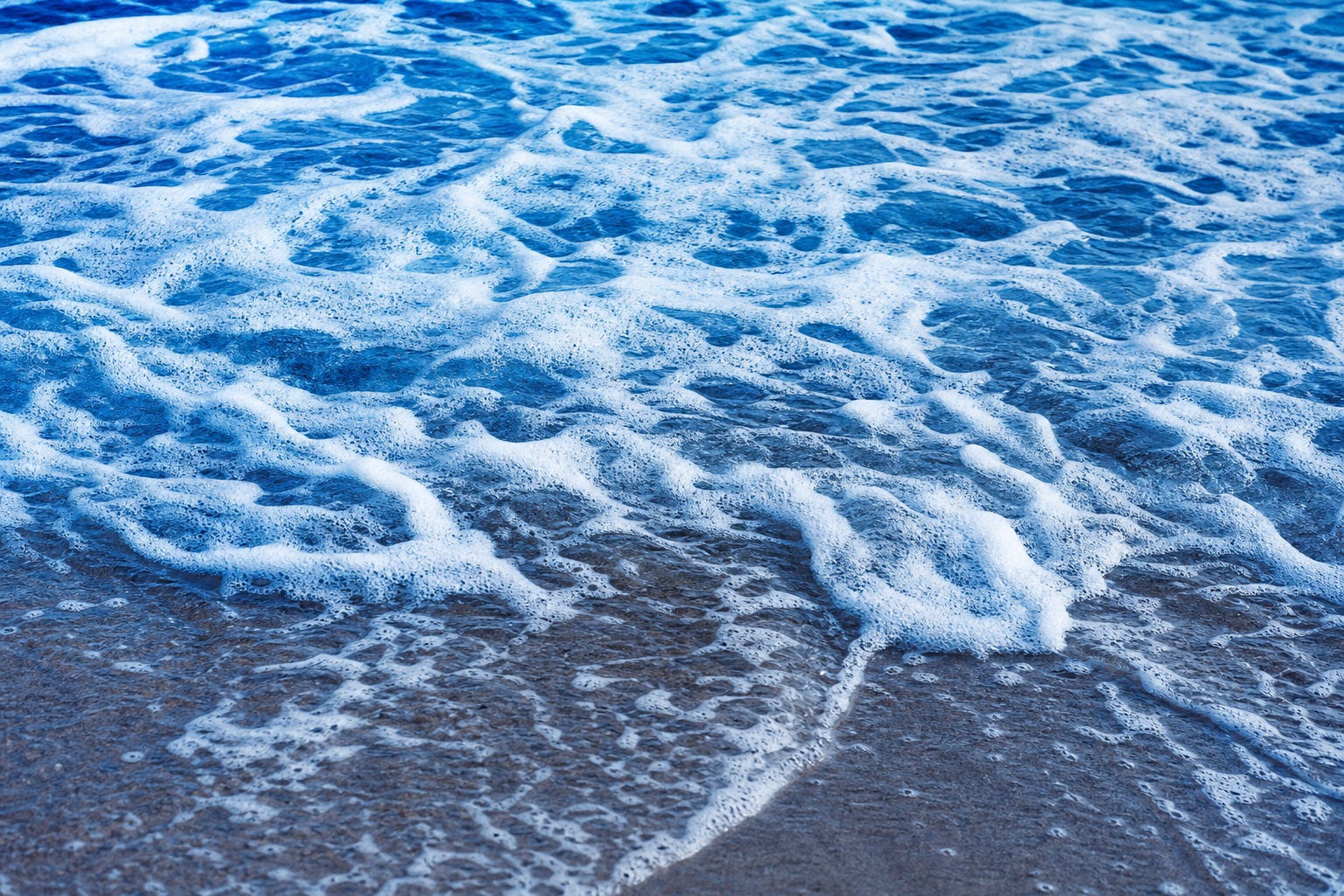 Blue ocean foam washing over a shoreline with textured white sea foam