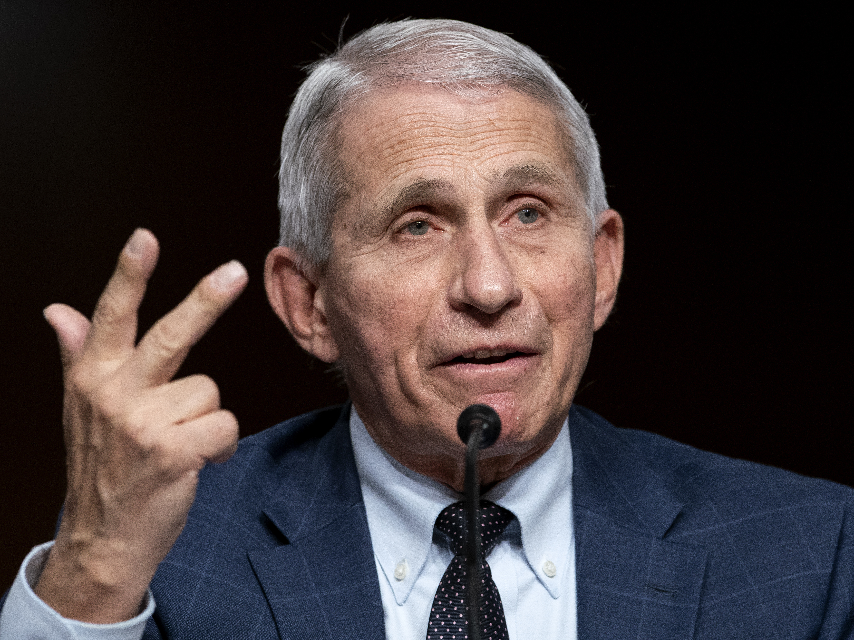 Dr. Fauci speaking at a microphone while gesturing with his hand