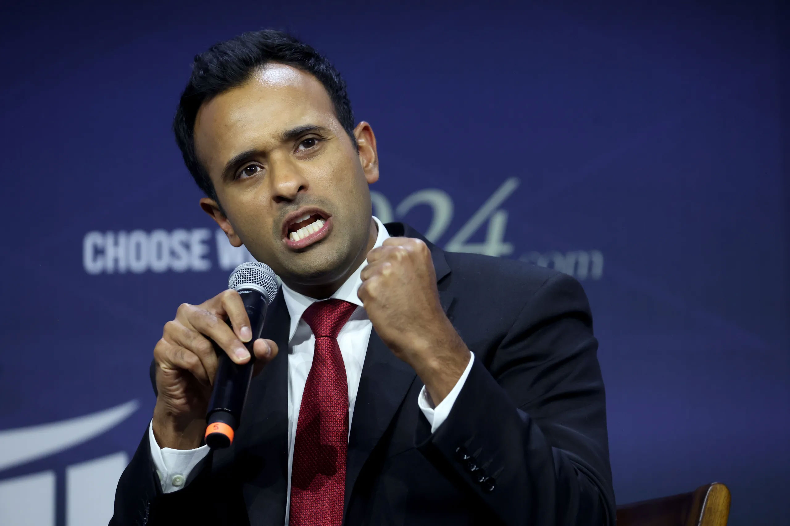 Man in a suit speaking onstage with a microphone at a conference