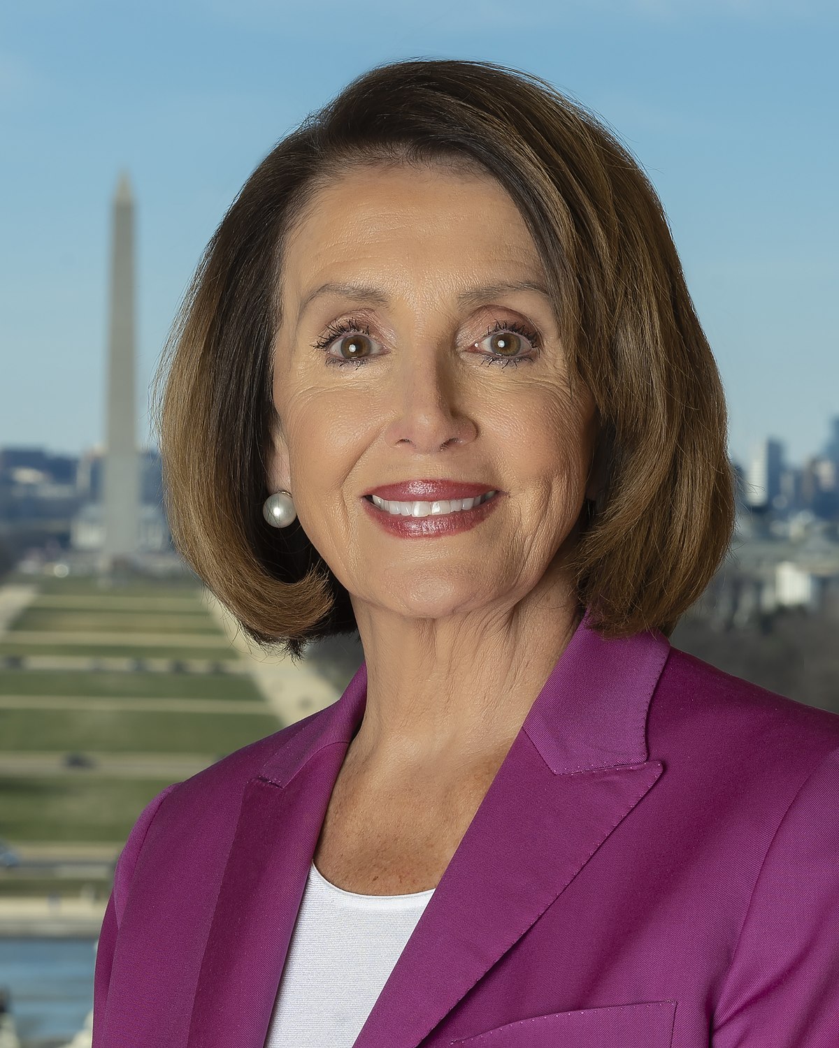 Smiling woman in a magenta blazer against a blurred city and flag background
