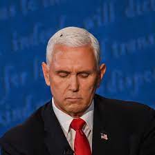 Mike Pence looking down against a blue debate-stage backdrop, wearing a dark suit and red tie.