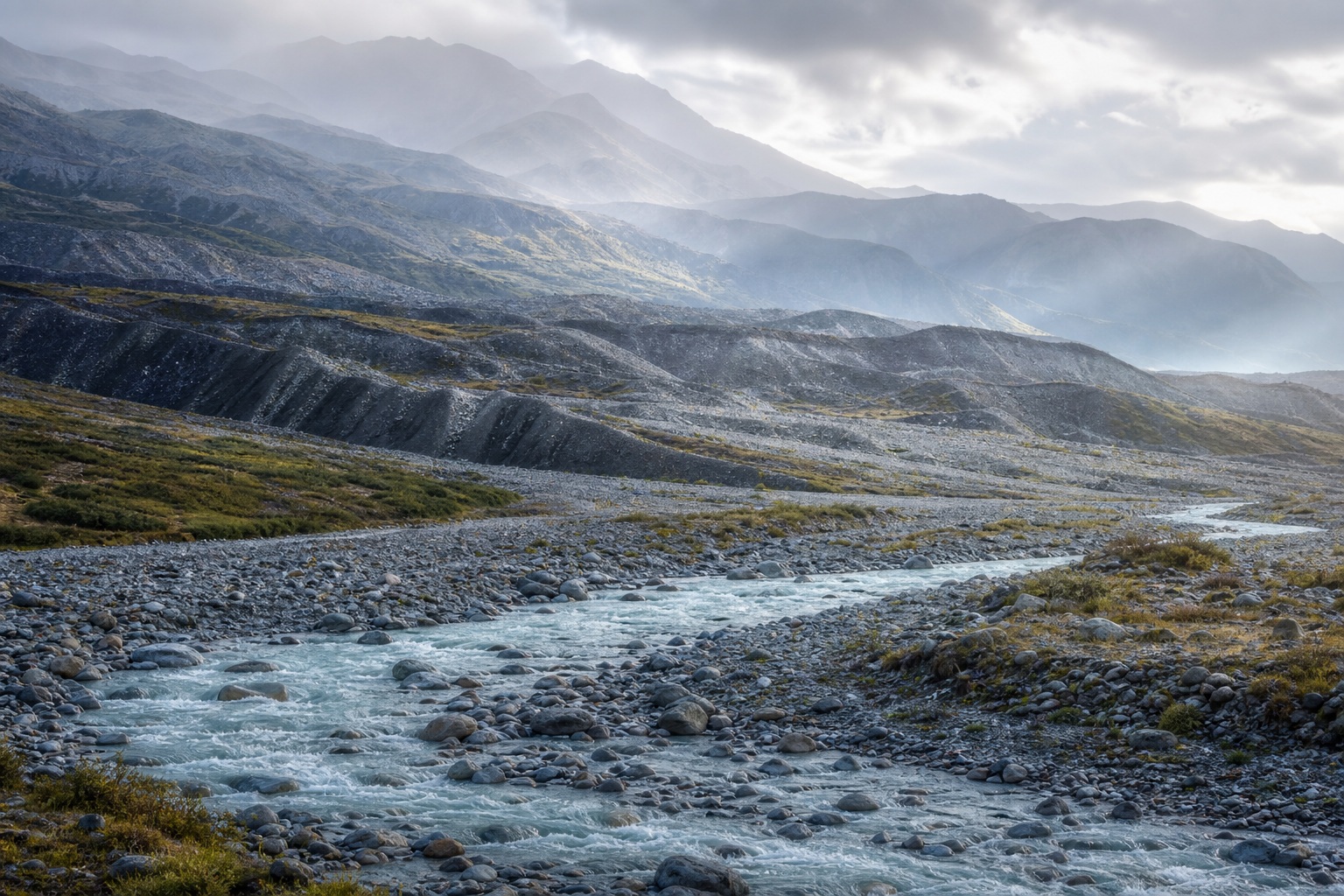 Glacial river winding through a mountain valley with layered ridges and cloudy dawn light