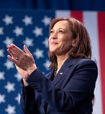 Kamala Harris clapping in front of a blurred American flag background.