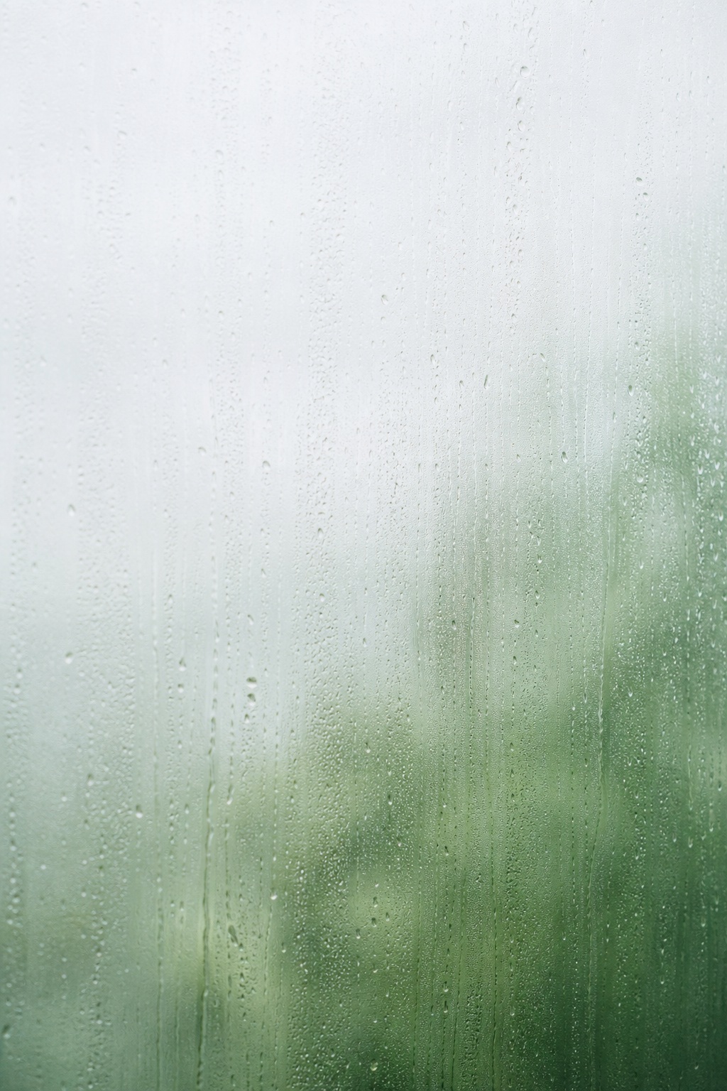 Misty rain-covered window with soft green bokeh blurred behind glass
