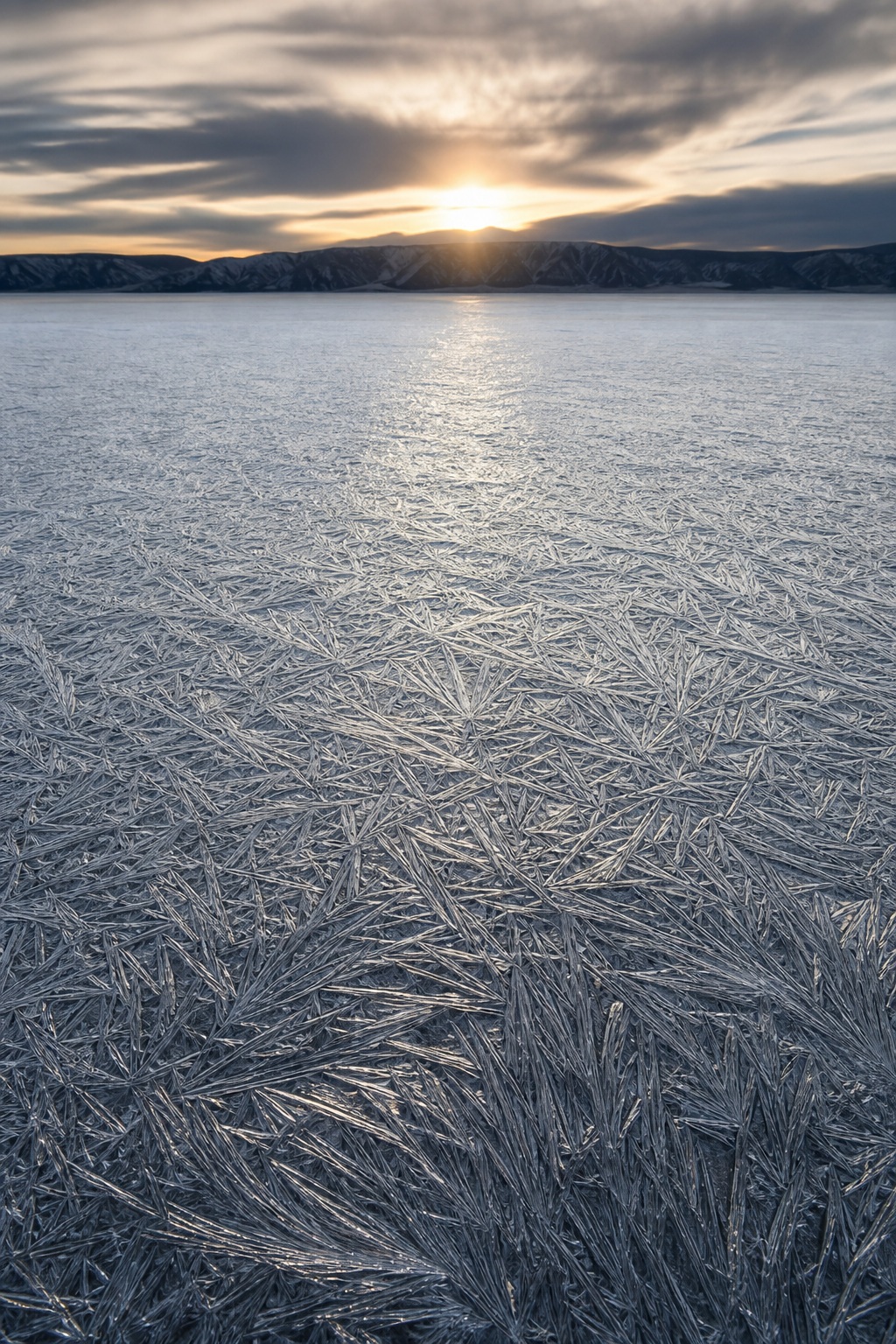 Frozen salt flat with etched mineral patterns and distant mountains under a low sun