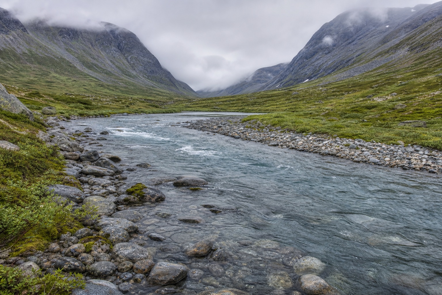 Glacial river winding through a rocky mountain valley under bright overcast skies.