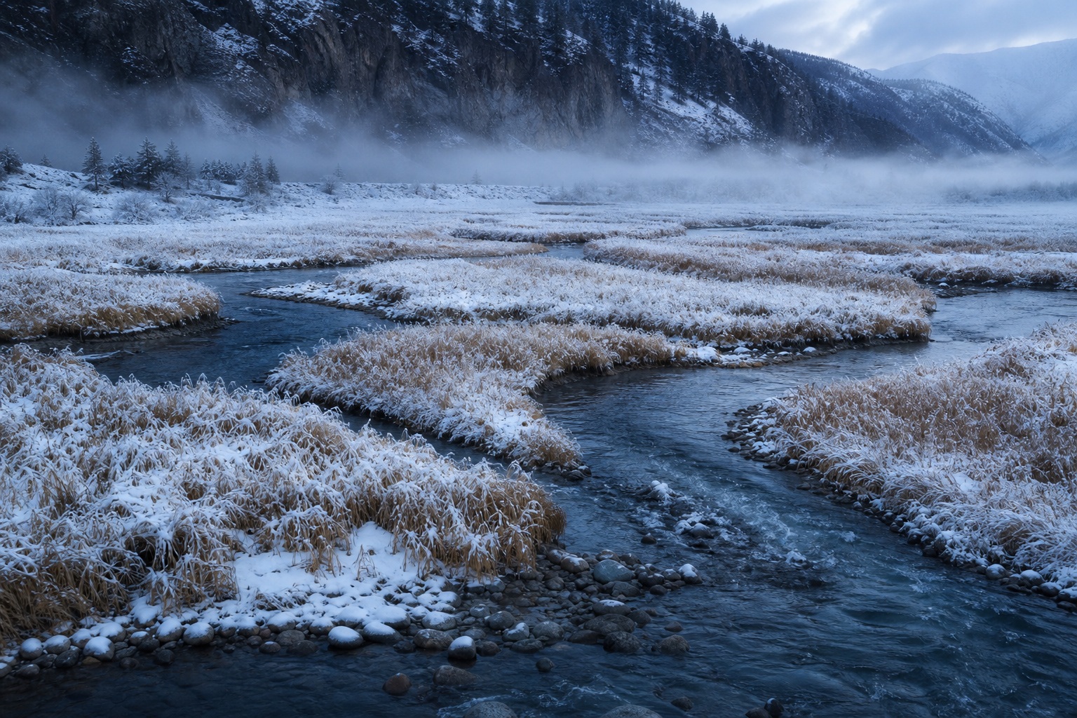 Snowy river valley with winding marsh channels, misty mountains, and snow covered grass