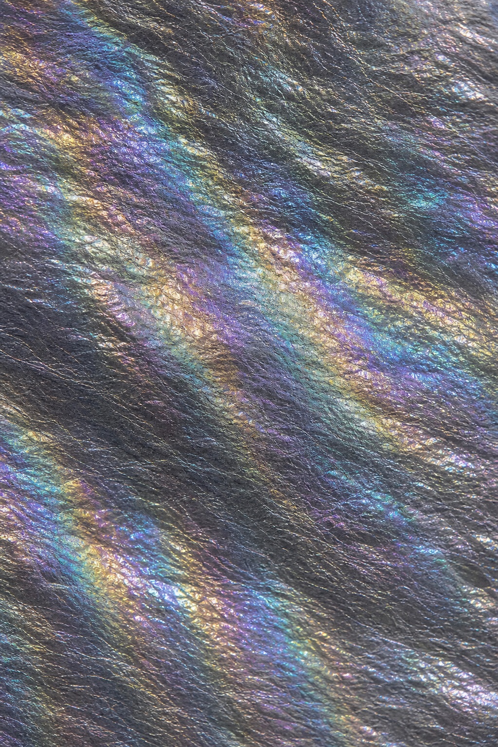 Abstract graphite foil surface with iridescent rainbow ripples and metallic shimmer.