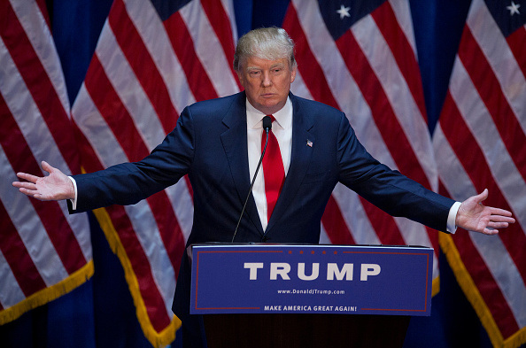 Speaker at a podium in front of multiple U.S. flags at a campaign rally