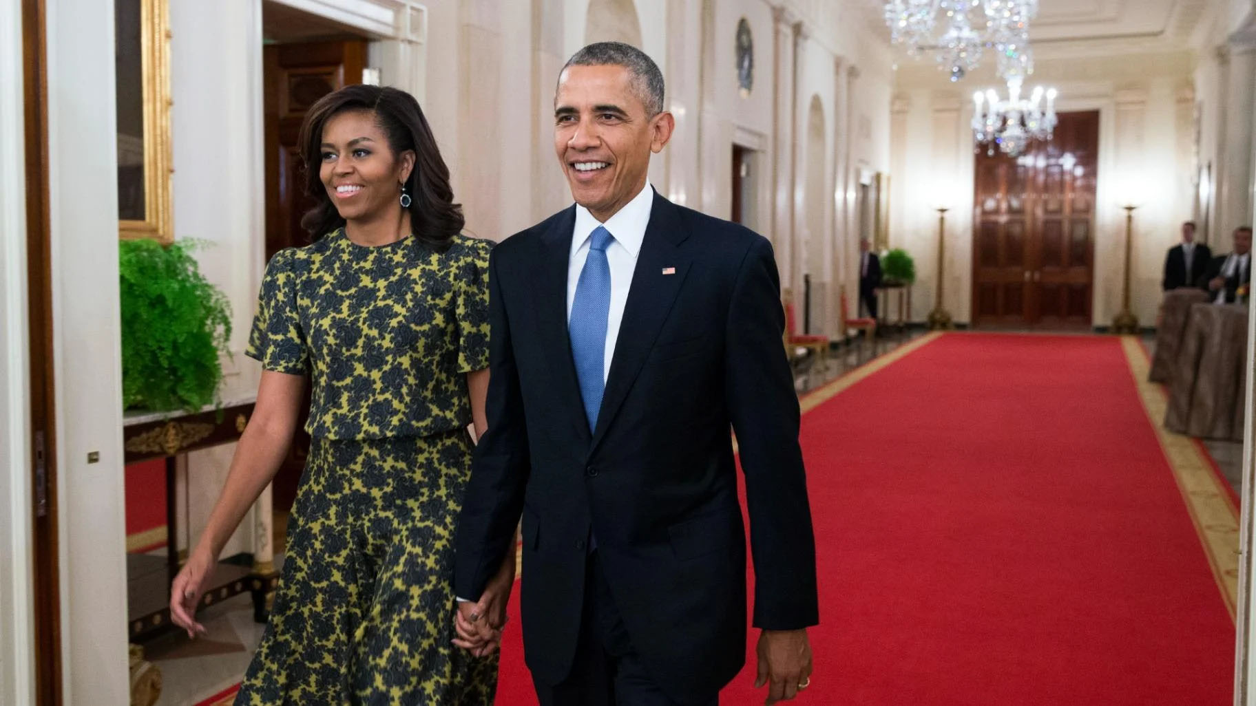 Barack Obama and Michelle Obama walking through a White House hallway on a red carpet.