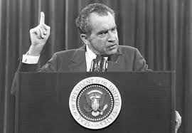 Black-and-white photo of Richard Nixon speaking at a podium with one finger raised.
