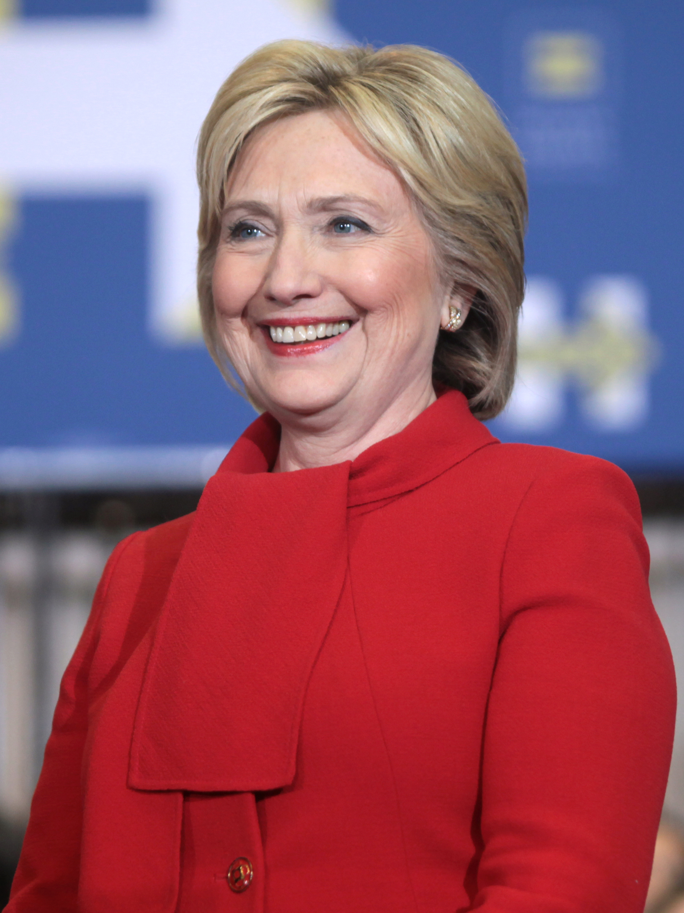 Smiling woman in a bright red coat against a blurred blue background.