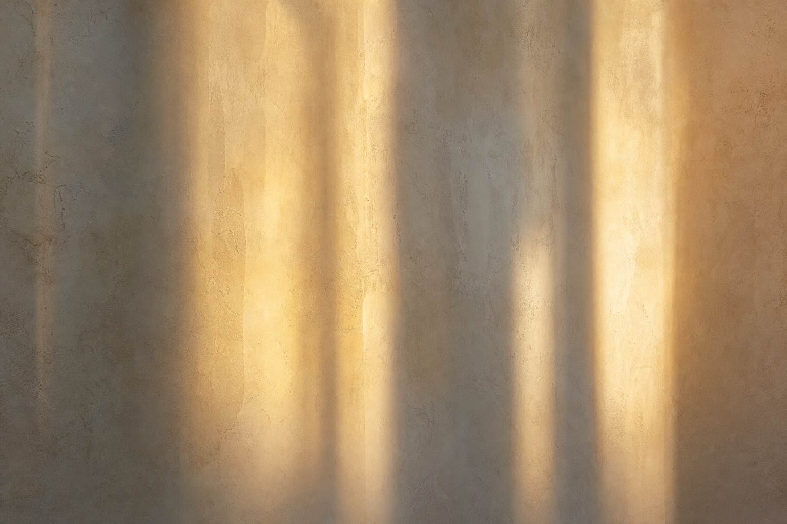 Vertical bands of soft golden light and shadow on a textured wall.