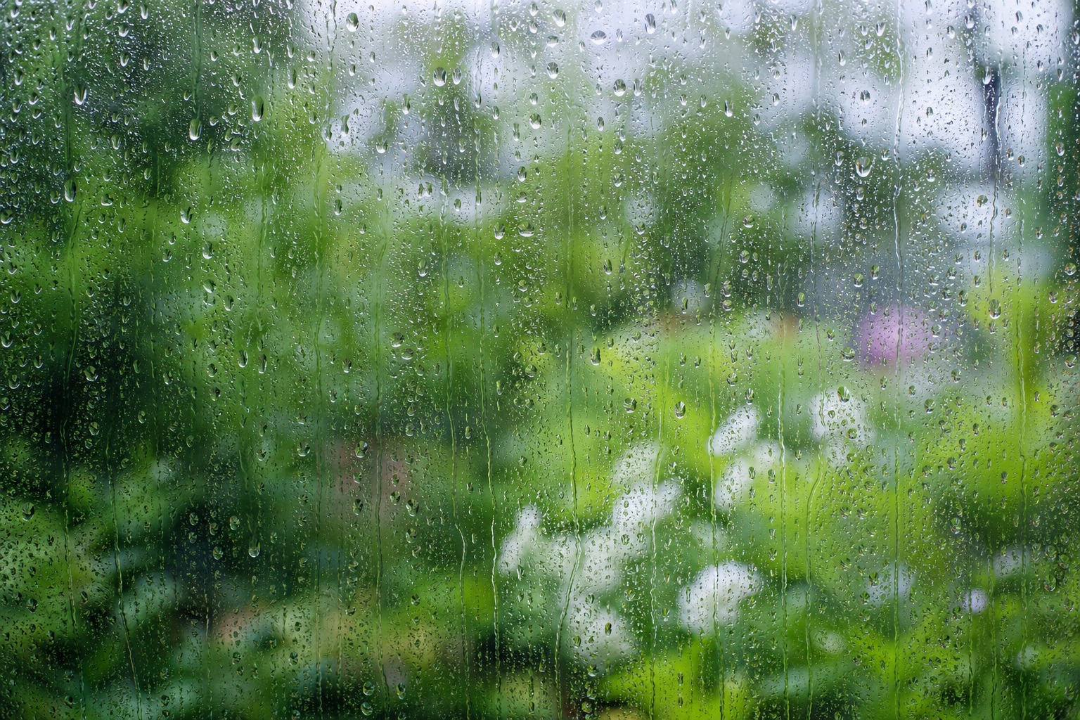 Raindrops on a window with a blurred green garden and soft bokeh lights.