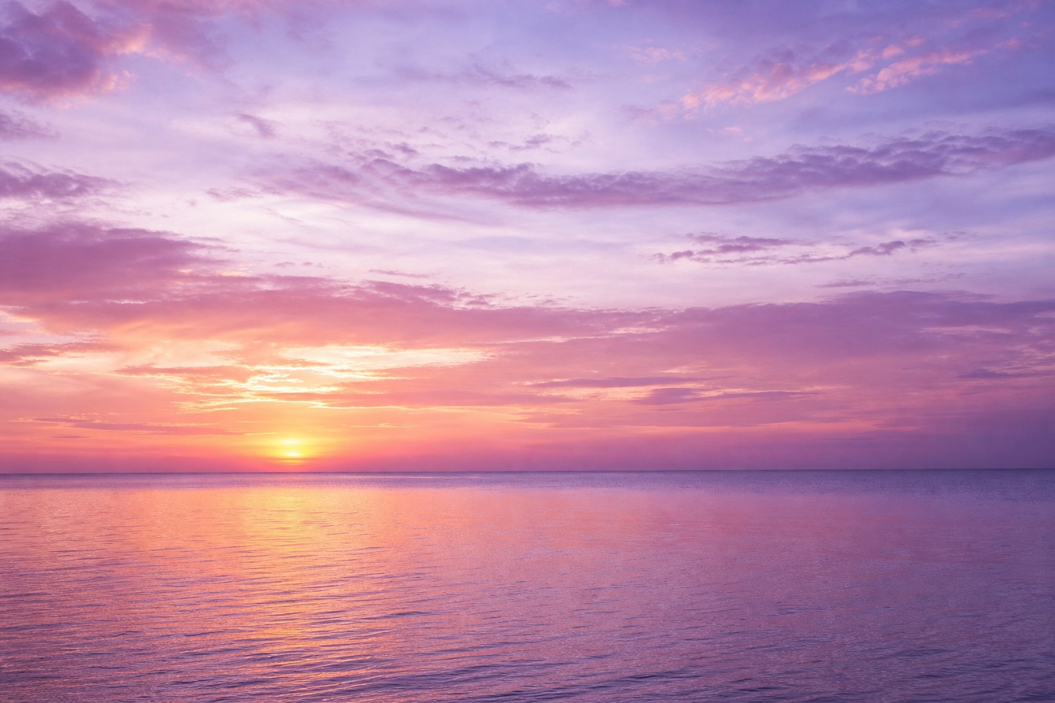 Lavender sunset over a calm ocean with glowing light near the horizon.