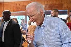 Joe Biden holding an ice cream cone indoors while people stand behind him.