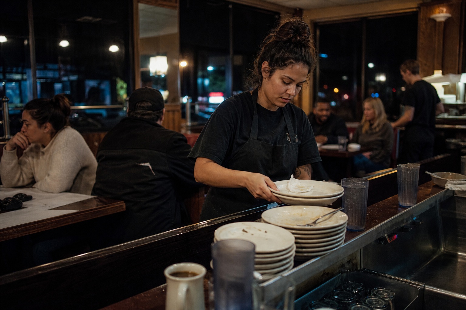 Person stacking plates at a diner counter during late-night cleanup.