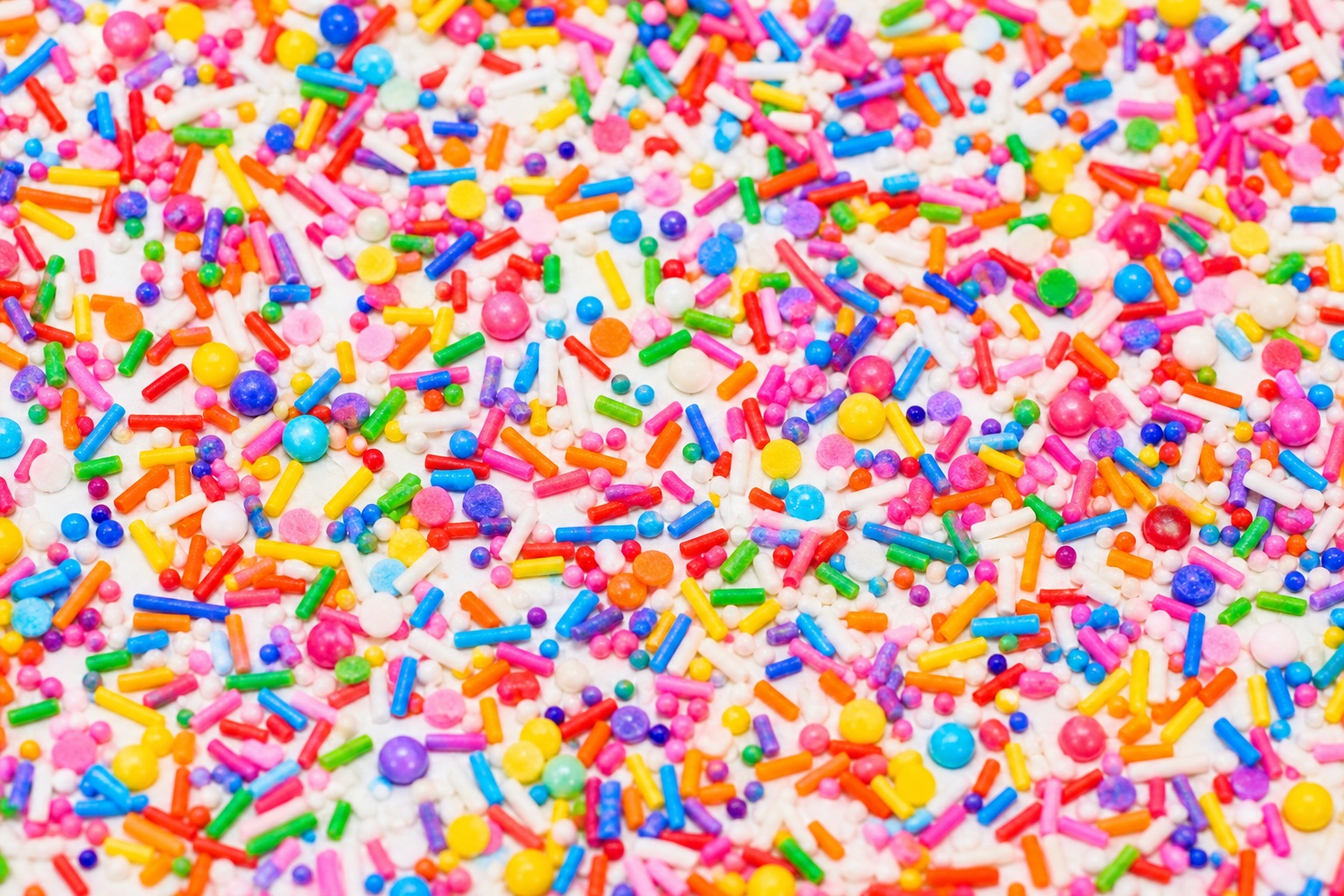 Colorful rainbow sprinkle confetti texture scattered across a white background.