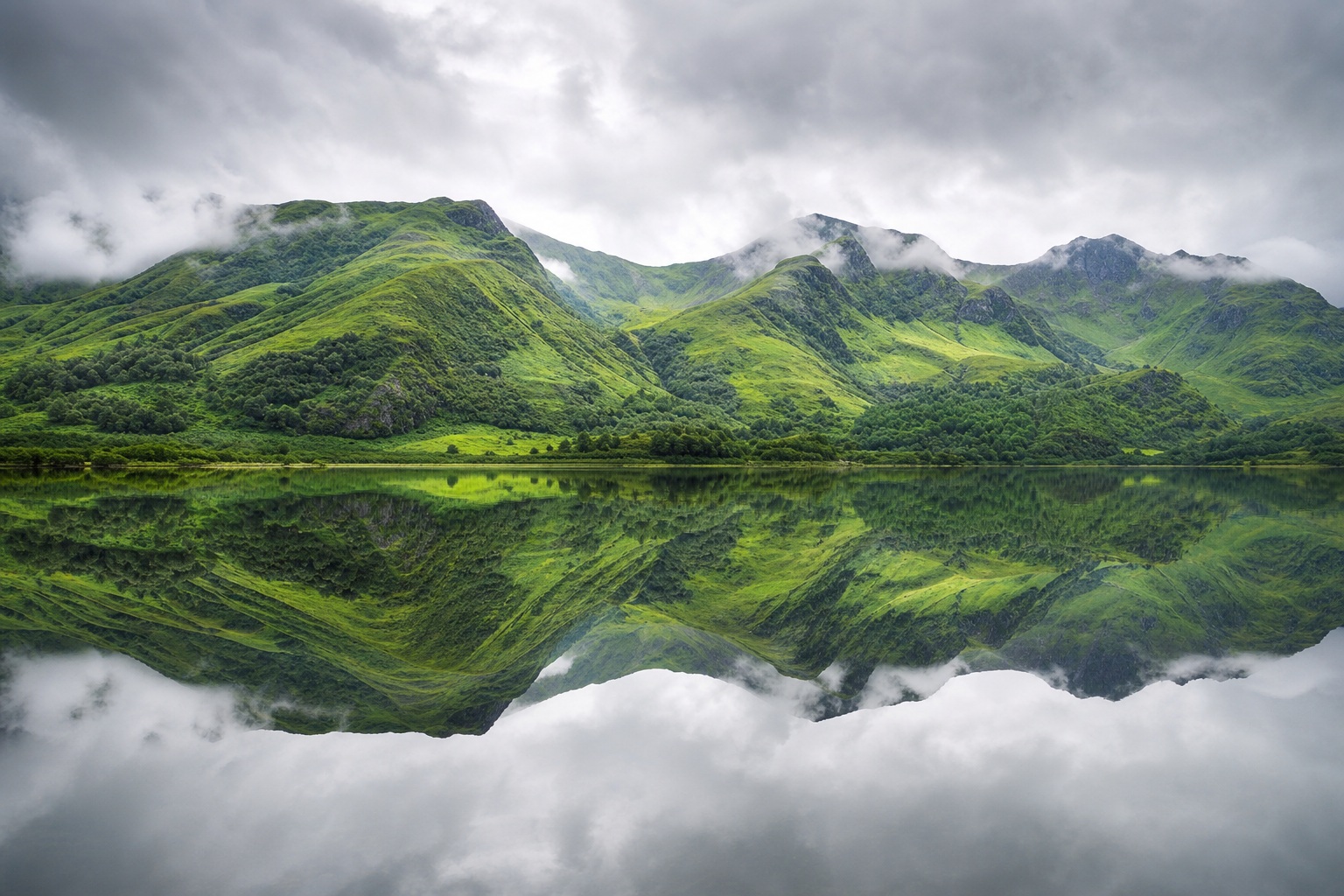 Green mountain range reflected in a calm lake under cloudy skies