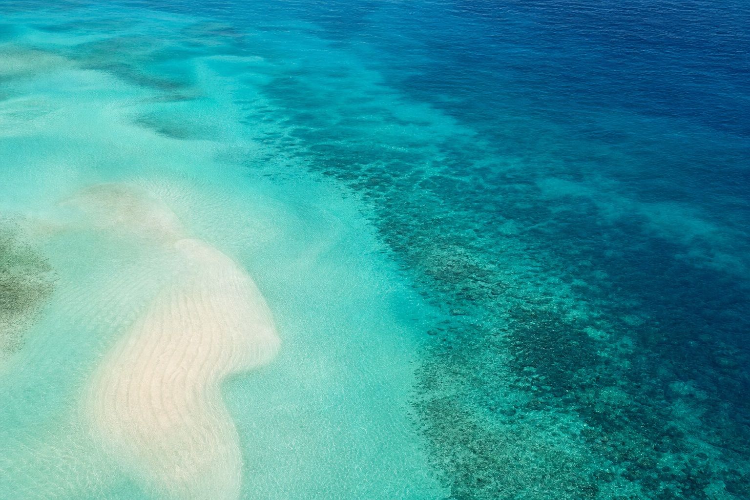 Aerial view of turquoise ocean water with soft coastal sand and gradient color changes.