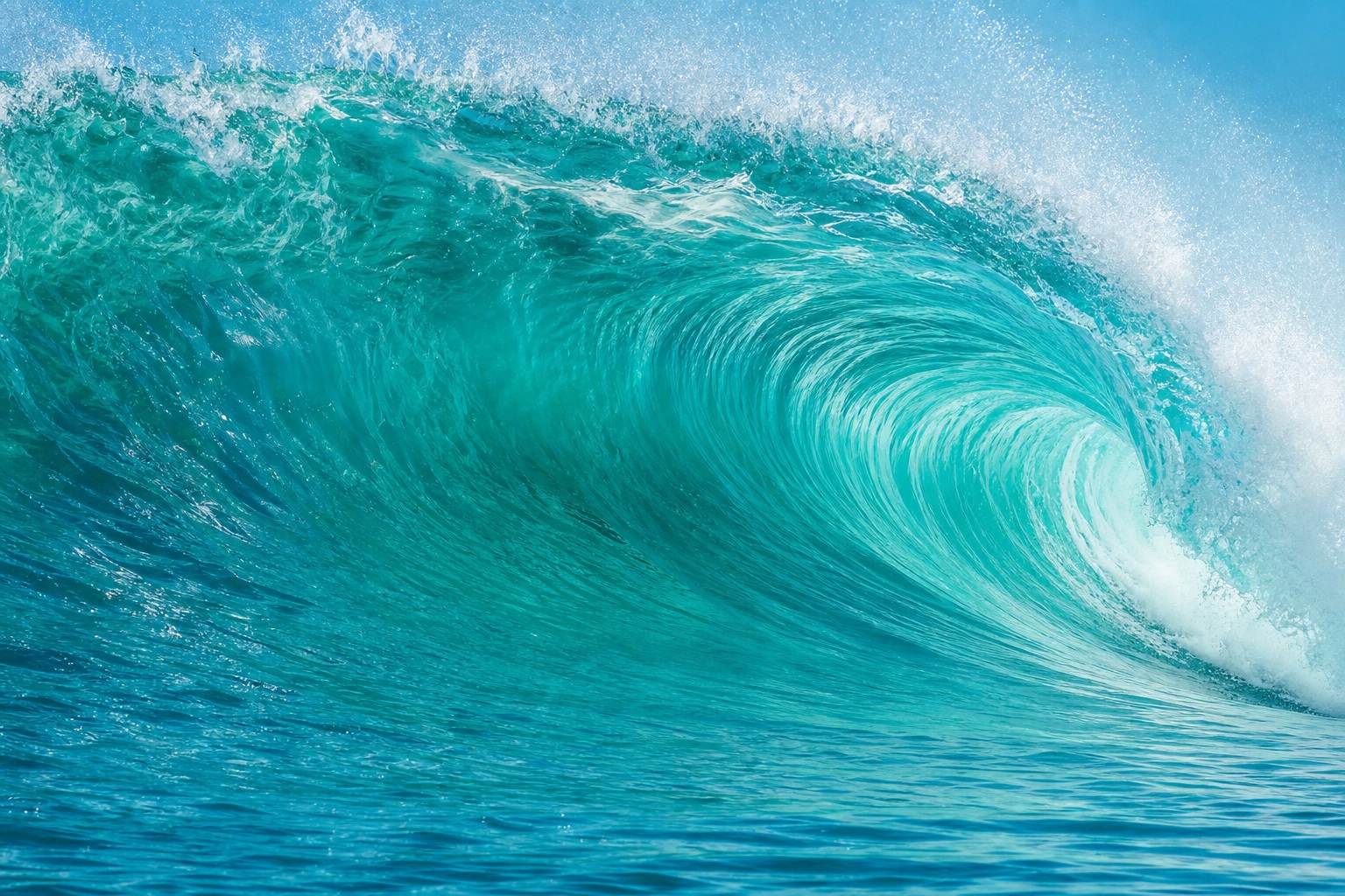 A curling turquoise ocean wave with white spray and deep blue water.