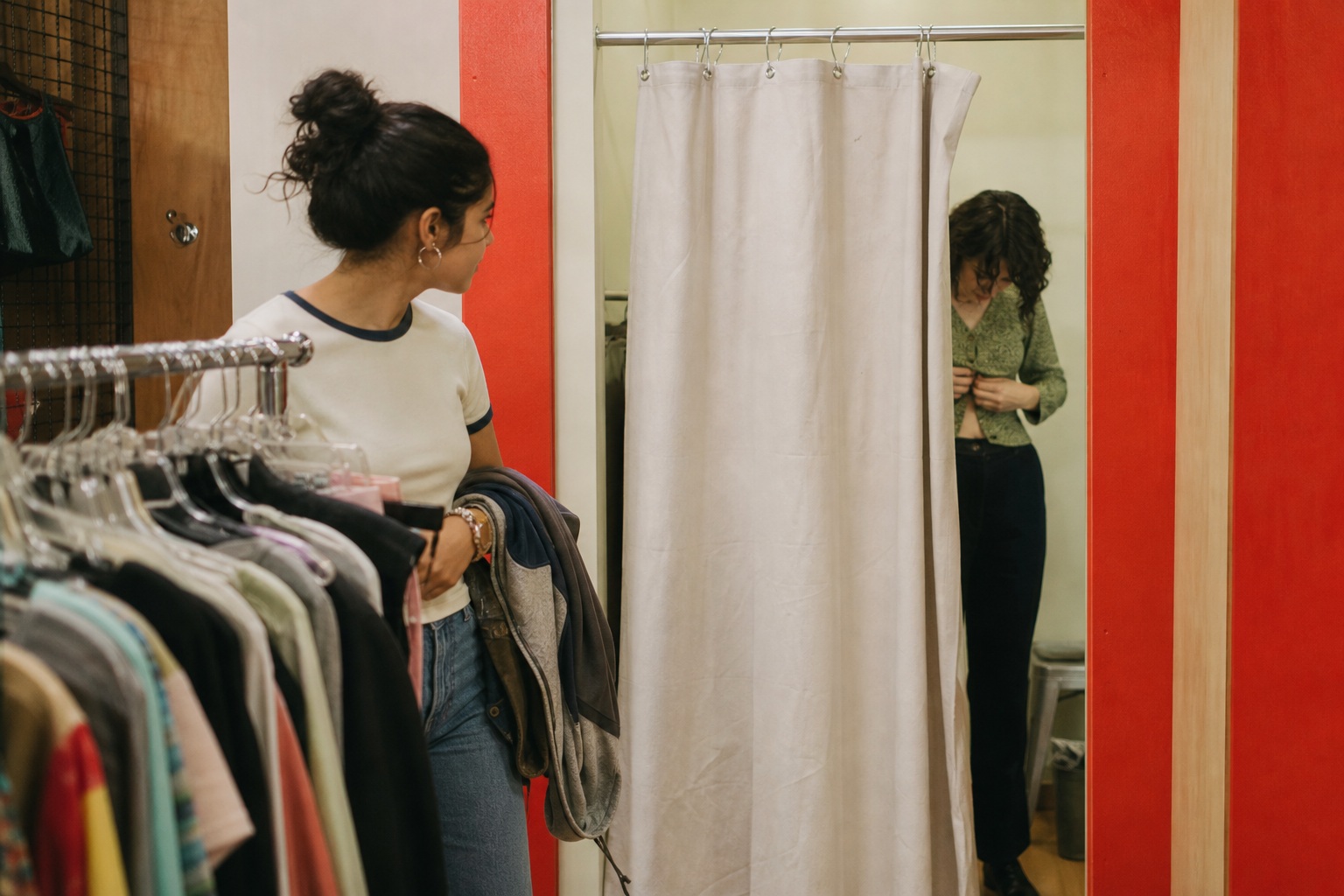 Person standing by a dressing room curtain in a thrift store beside racks of vintage clothes.