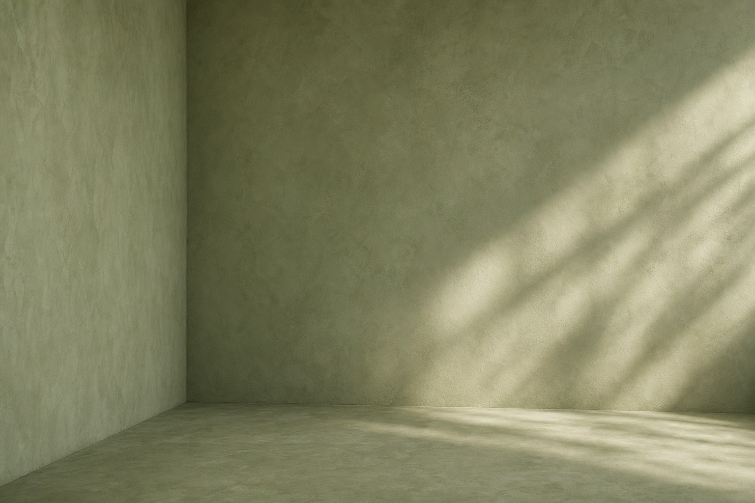 Empty sage-green studio corner with soft light and diagonal shadow across the wall and floor.