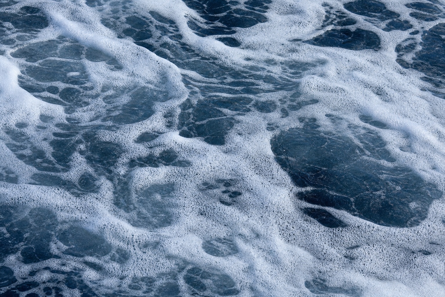 Blue ocean water with white sea foam swirling across the surface