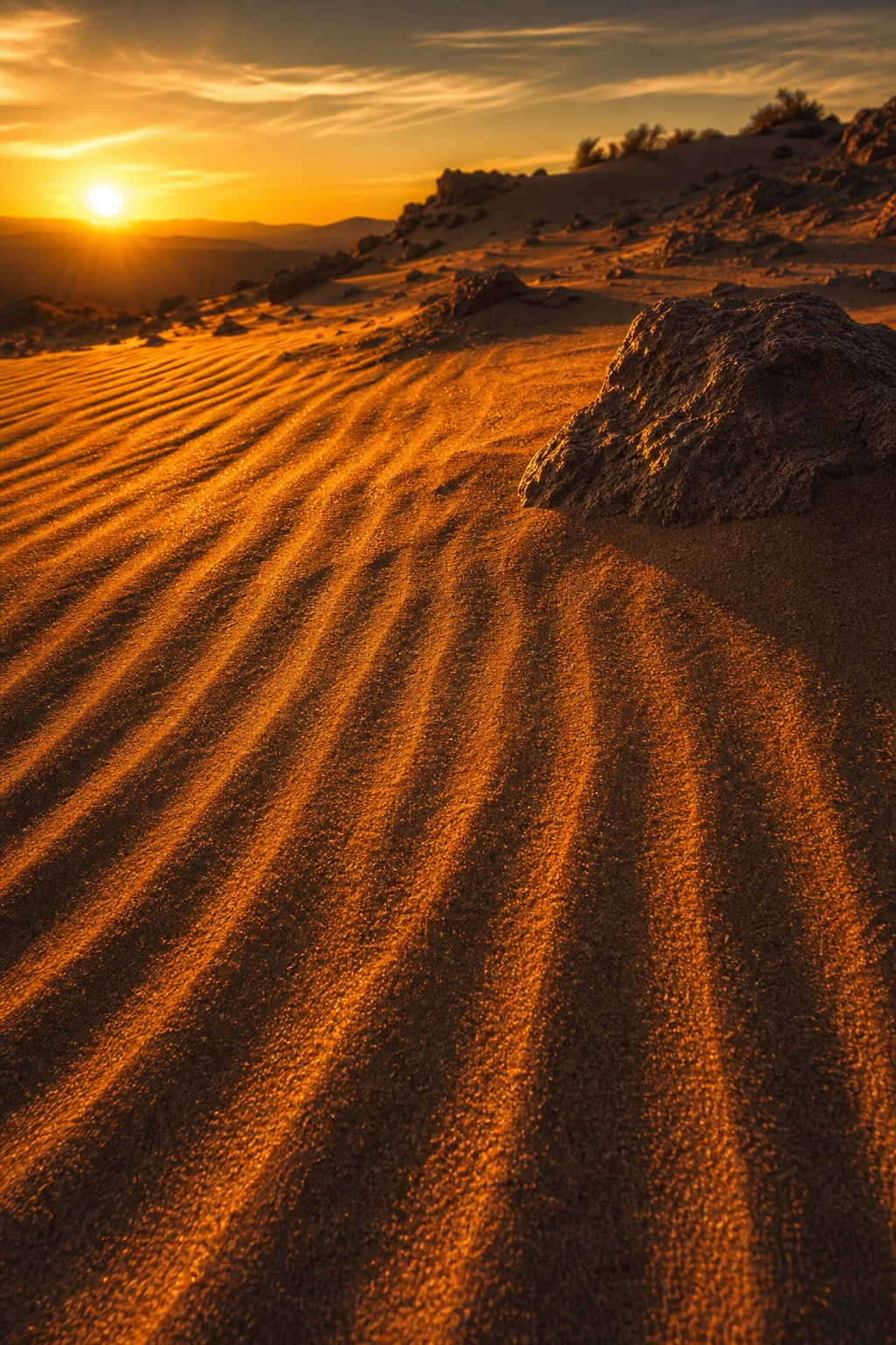 Golden desert dunes with rippled sand under a glowing sunset sky