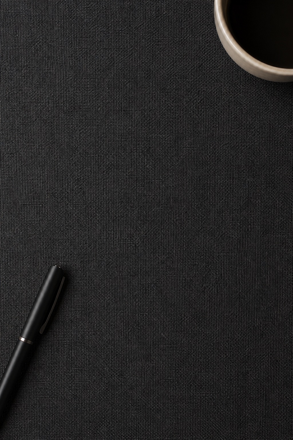 Vertical charcoal fabric desk surface with a pen and part of a cup at the edge.