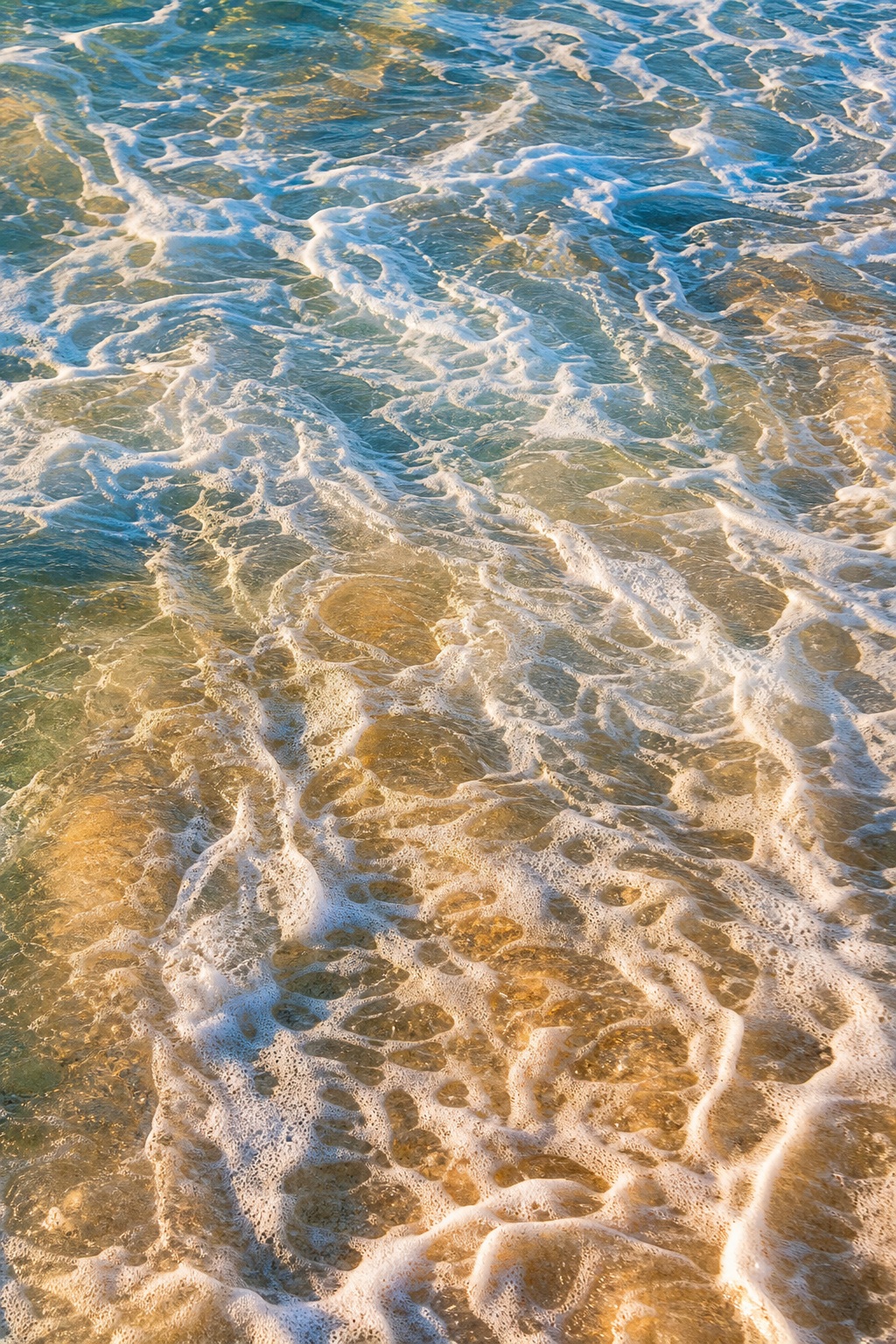 Swirling whitewater and sea foam over shallow ocean water with warm golden light