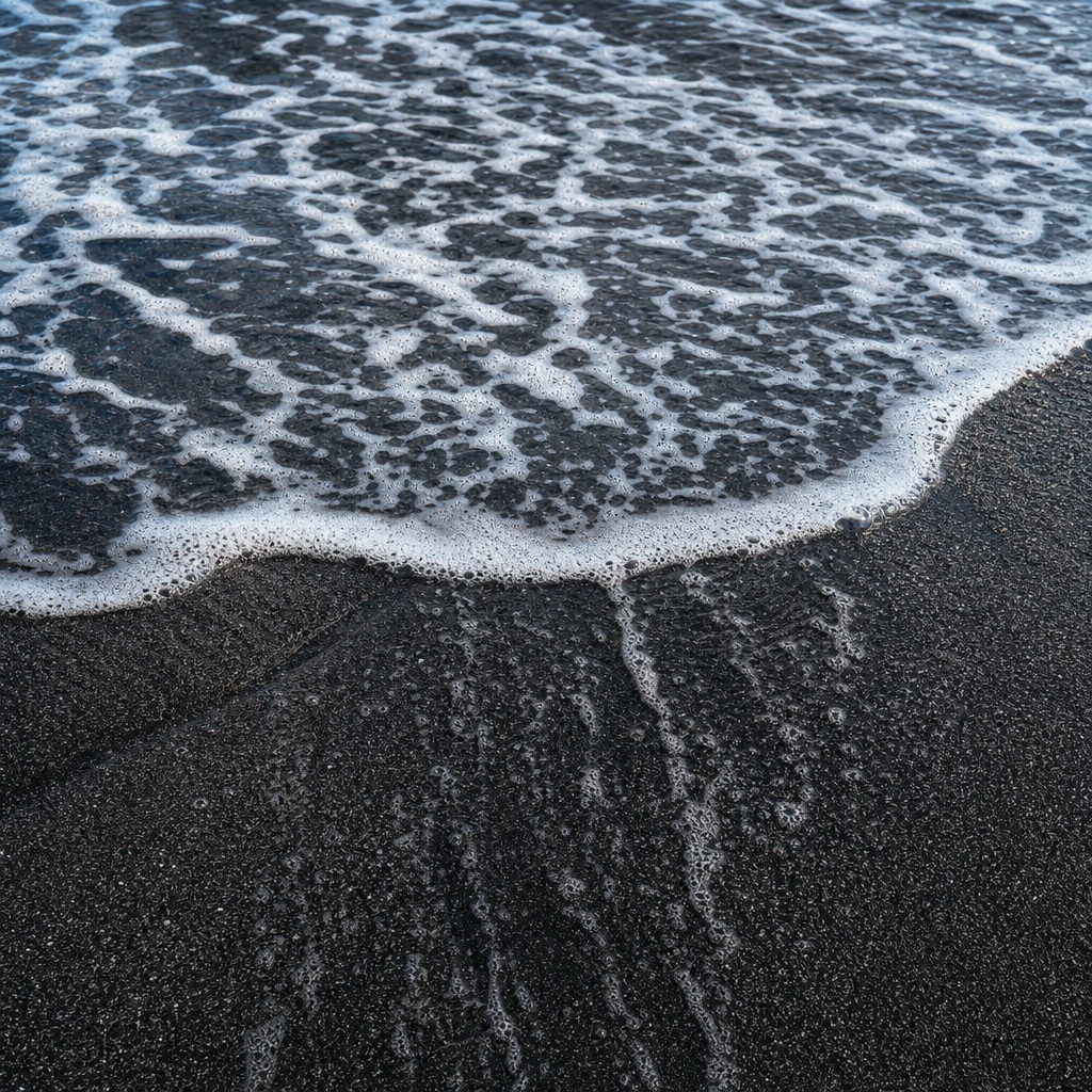 Seafoam washing over a black sand beach shoreline with ocean texture