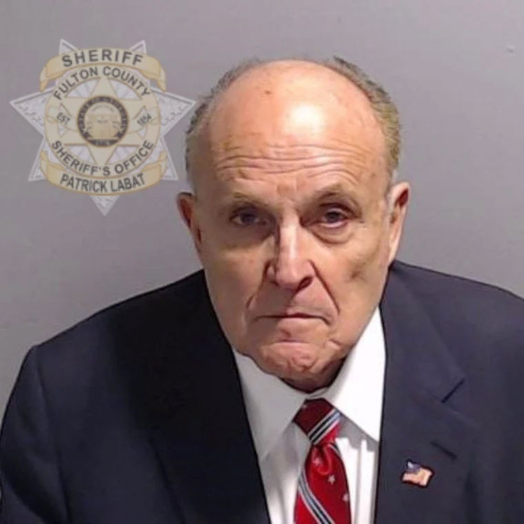Mugshot-style portrait of an older man in a suit with a sheriff office emblem behind him.