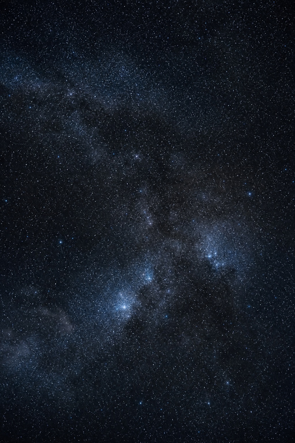 Silver blue star field with a faint distant light cluster in a dark night sky.
