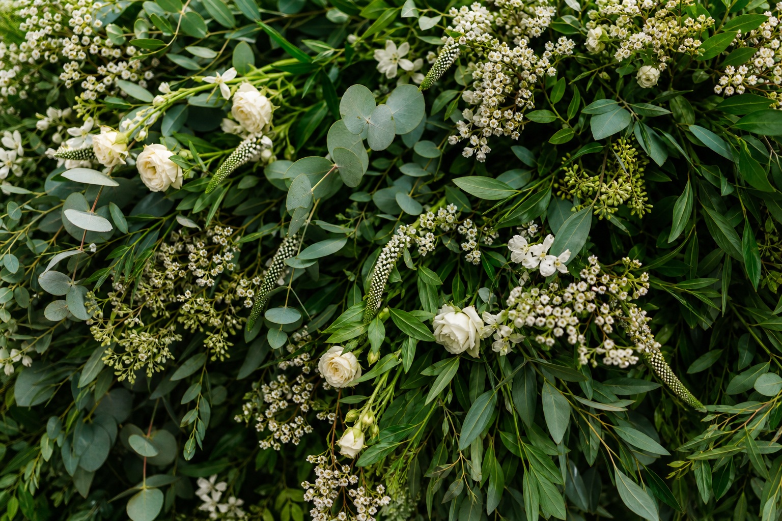 Close view of eucalyptus leaves, white flowers, and dense greenery garland.