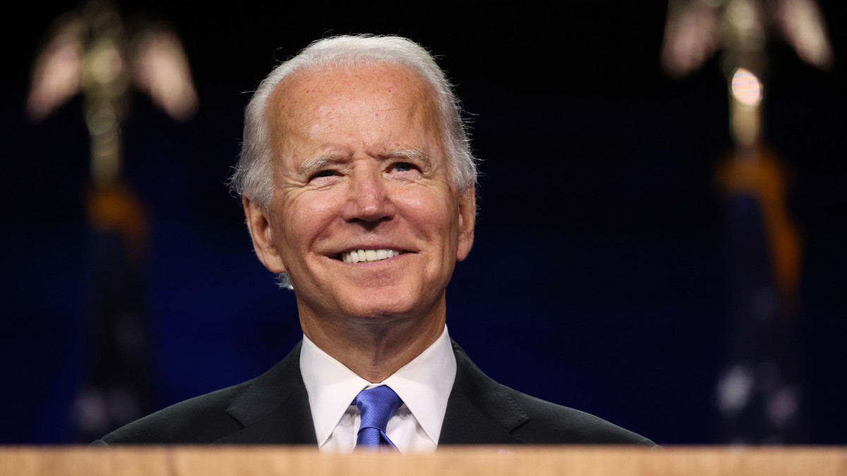 Joe Biden smiling behind a podium on a dark stage background.
