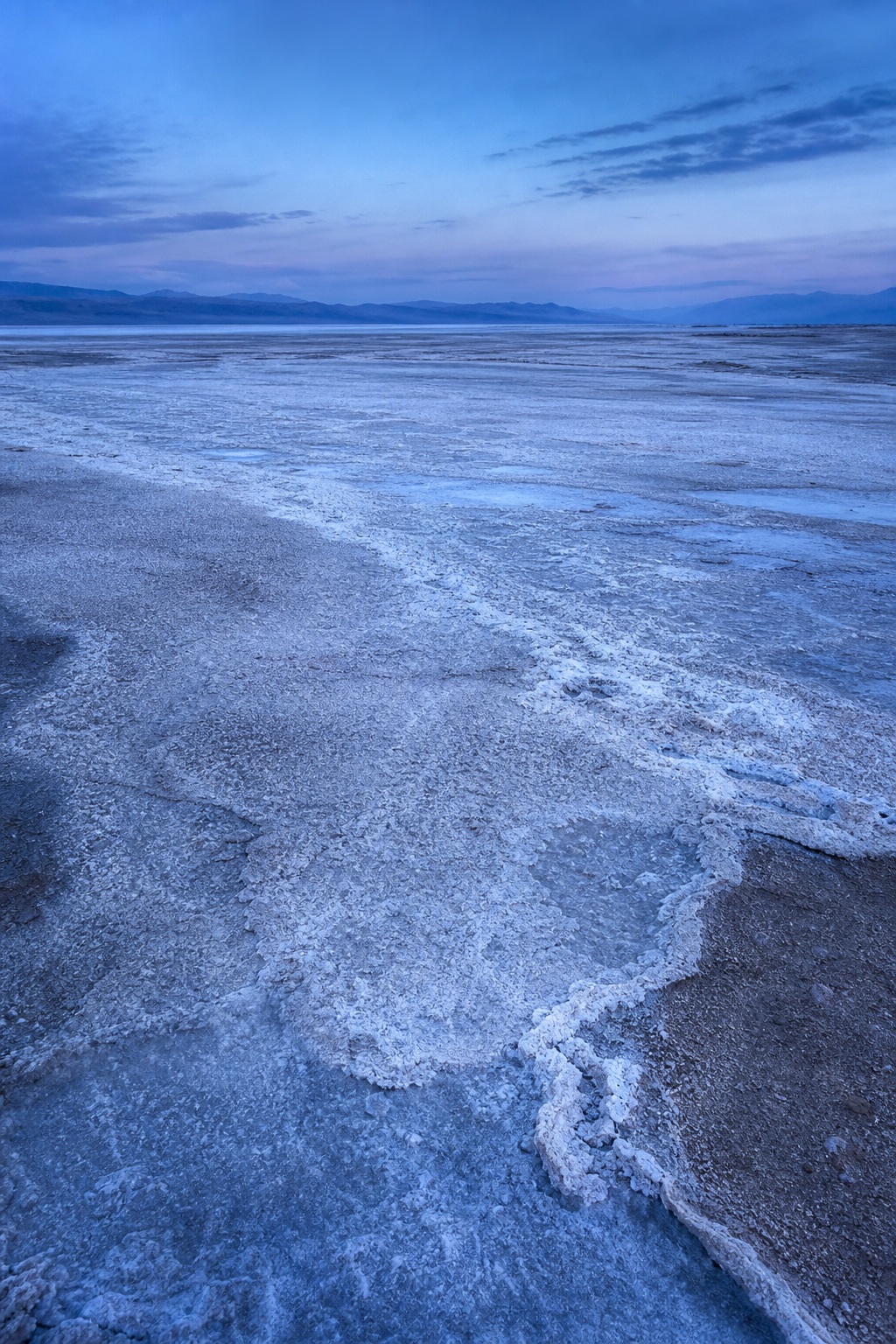 Blue twilight over a textured salt flat with a distant basin and cloudy sky.