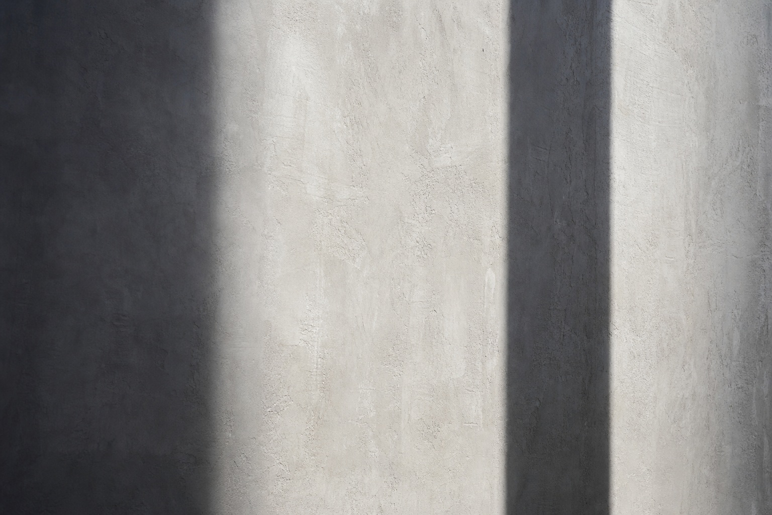 Light gray wall with two dark vertical shadows creating an abstract architectural composition.