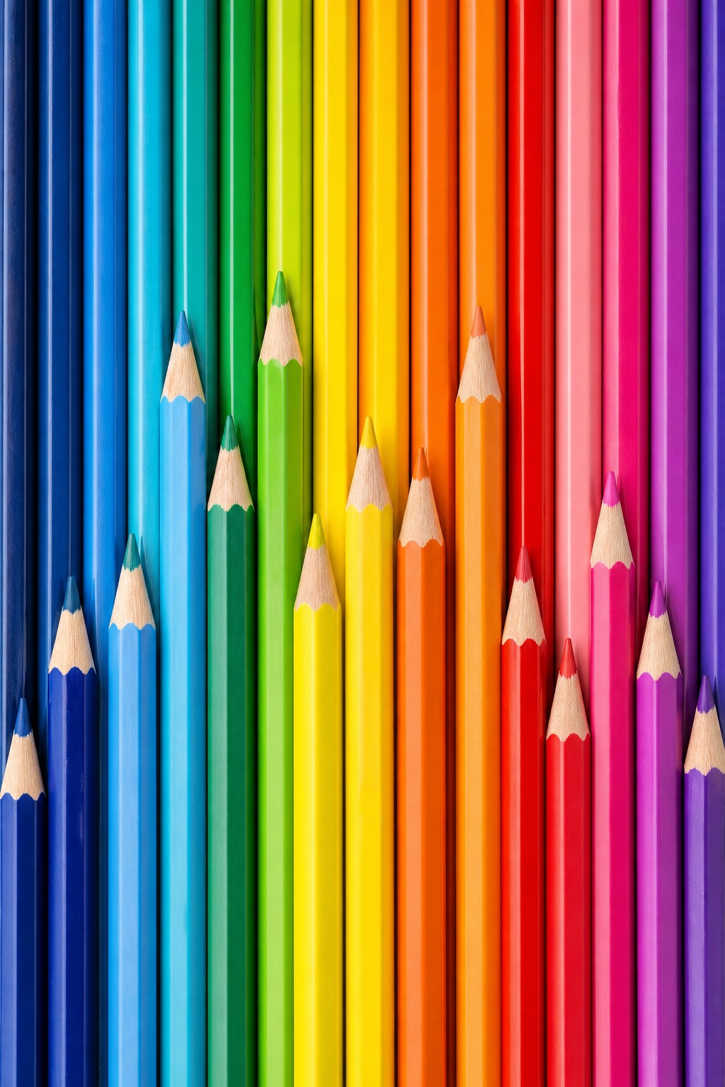 Row of colored pencils arranged vertically in a rainbow gradient texture.