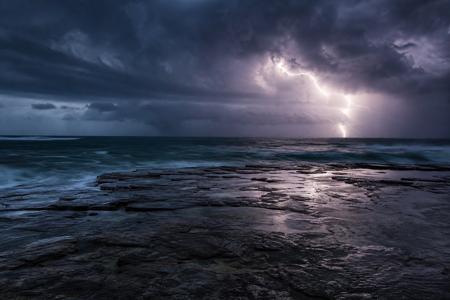 Lightning flashing over a stormy ocean and rocky shoreline under dark clouds