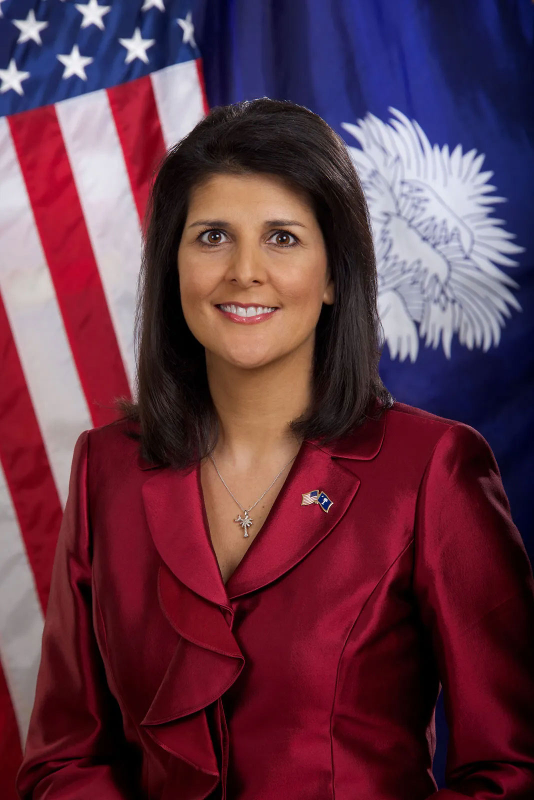 A woman in a maroon blazer posing in front of American and South Carolina flags.