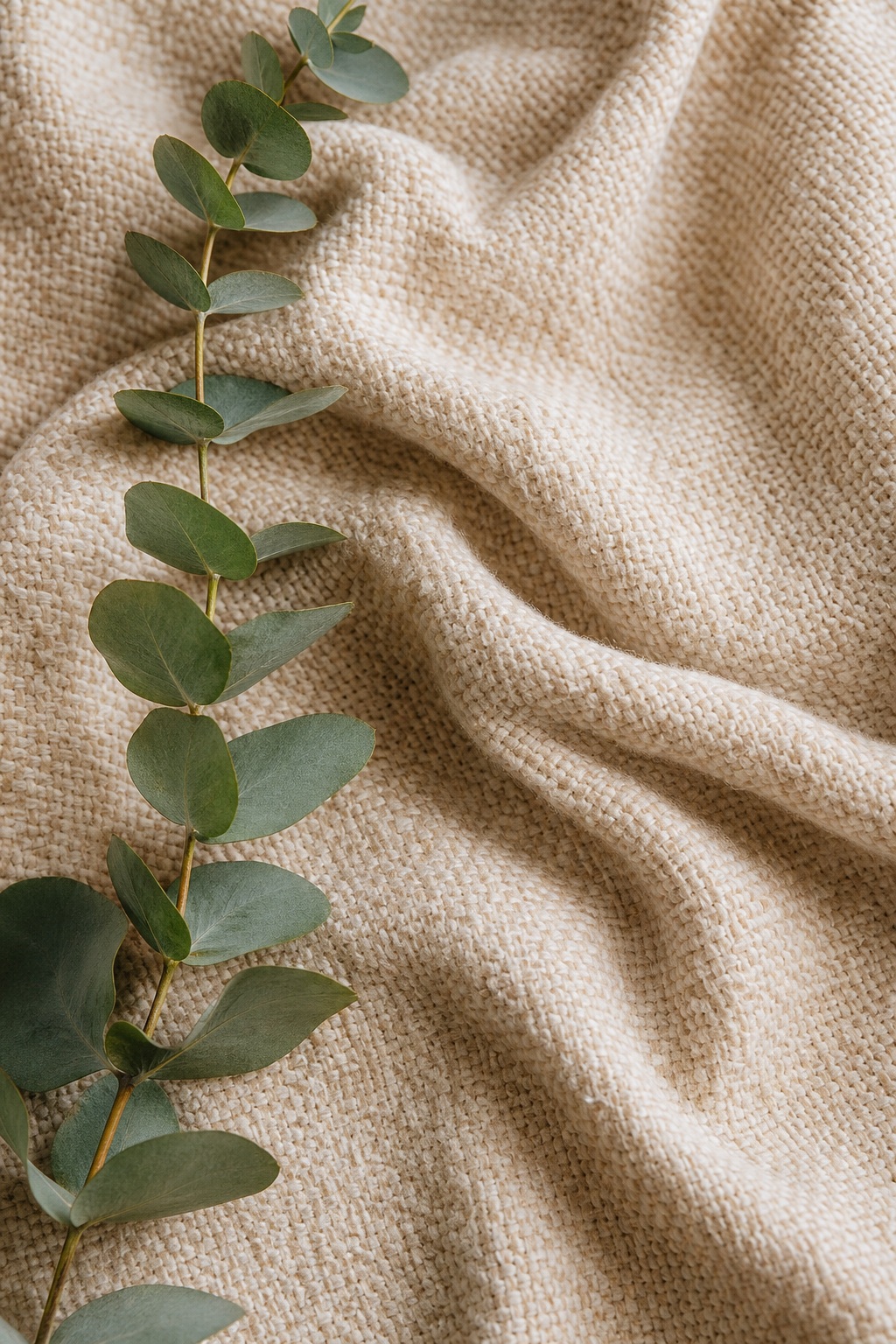 Vertical woven fabric texture with eucalyptus leaves along the left edge