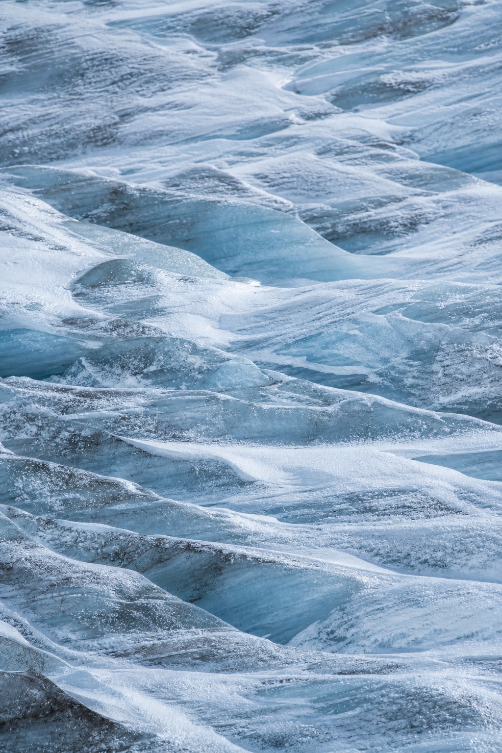 Wind-scoured blue glacier ice with layered snow and crevasse-like texture