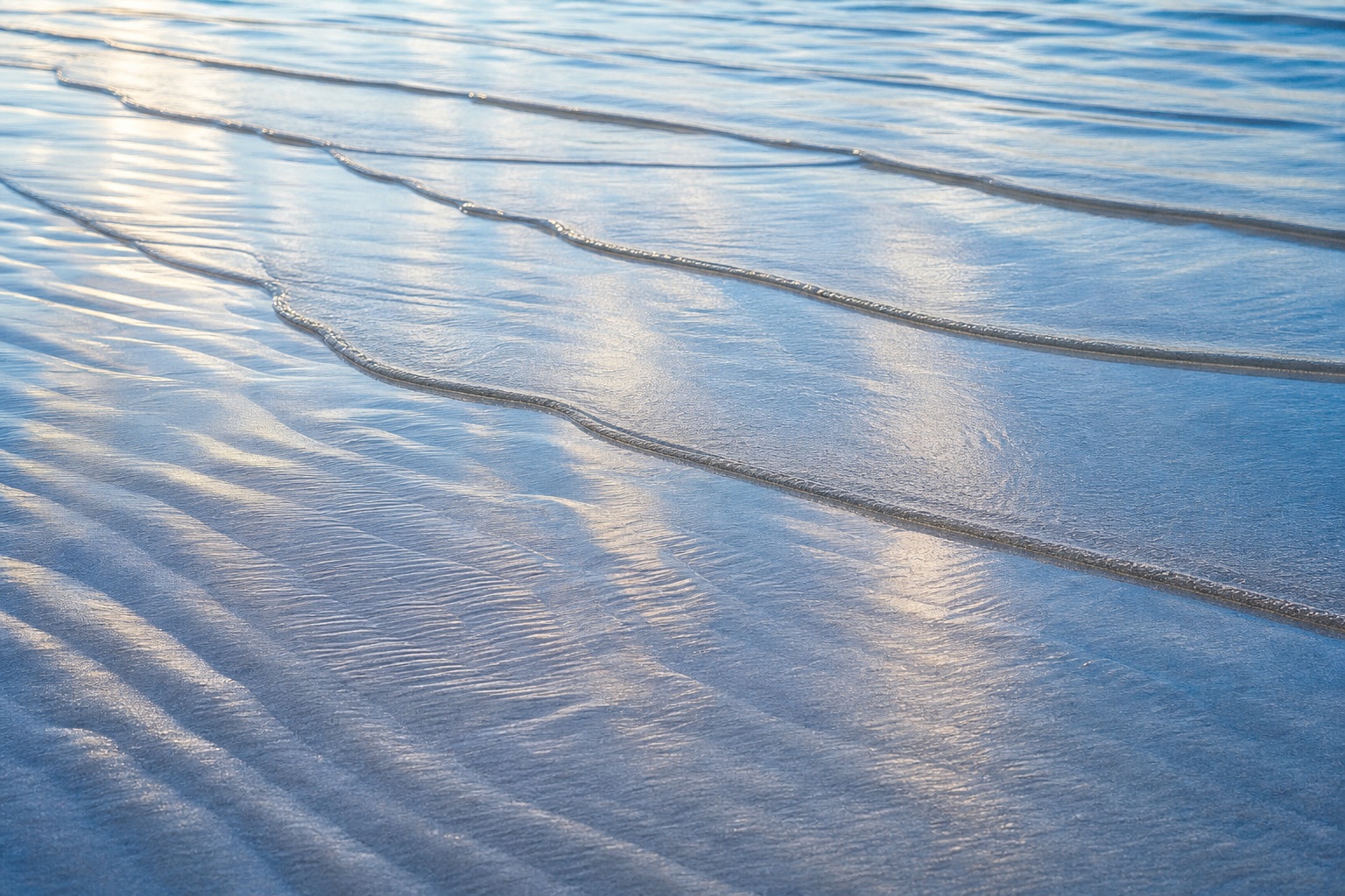 Silver blue ocean water with gentle tide ripples over wet sand